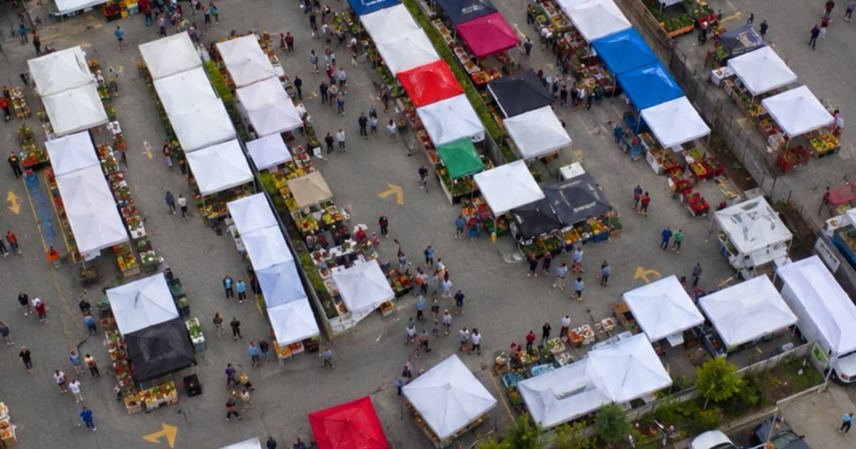 Aerial view of a bustling farmers market with rows of colorful vendor tents