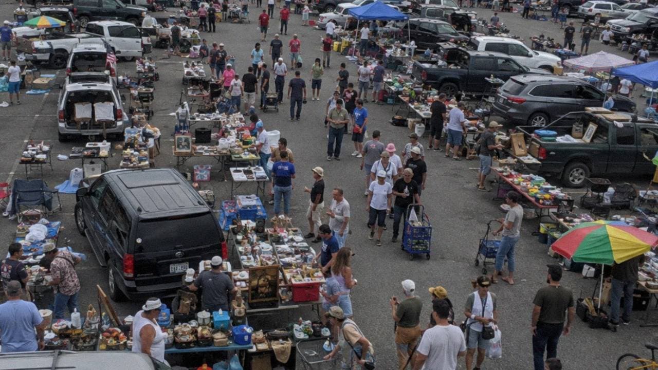 Aerial view of a busy outdoor flea market with rows of vendor tables and shoppers browsing