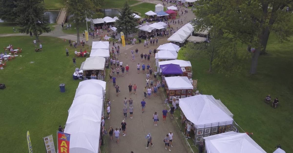 Aerial view of a large outdoor art fair with rows of white vendor tents and crowds of visitors